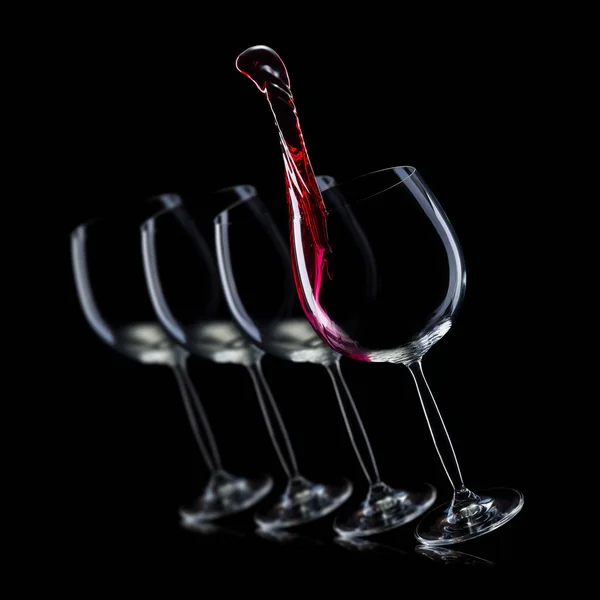 Set of empty glasses for red wine with splashes in a row isolated on black background. — Stock Photo, Image