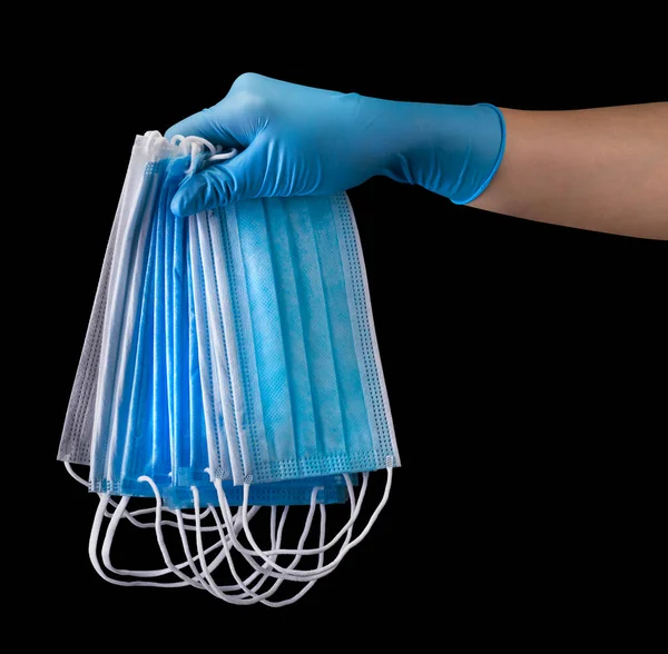 Doctors hand in medical gloves holding a pile of masks isolated on black — Stock Photo, Image