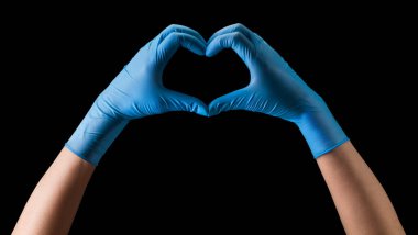 Doktor 'un eli steril tıbbi eldivenlerle siyah arka planda izole edilmiş kalp şeklini gösteriyor. Salgın ve virüslere karşı korunma kavramı.