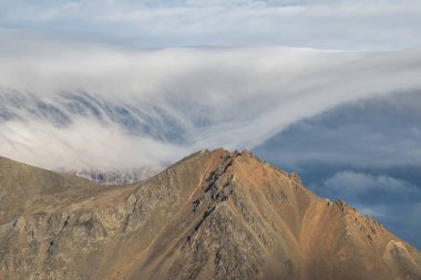 Göz kamaştırıcı kayalık karlı dağların fotoğrafları alçak, güzel, gri bulutlar.