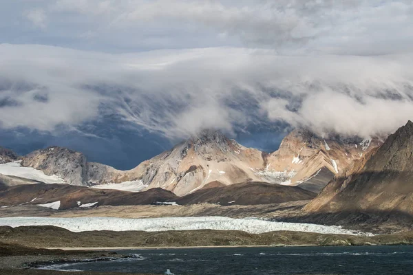Göz kamaştırıcı kayalık karlı dağların fotoğrafları alçak, güzel, gri bulutlar.