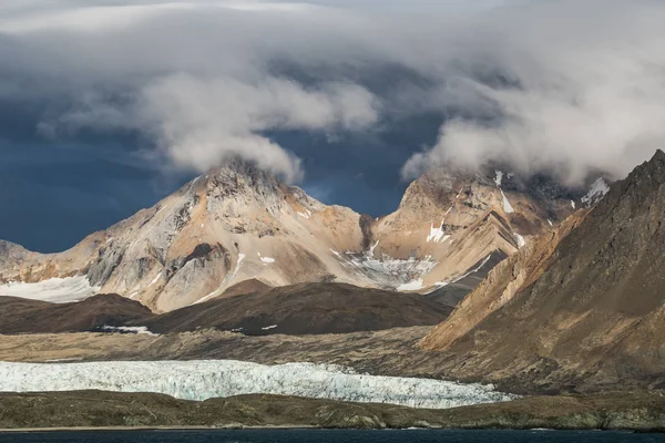 低い灰色の雲と豪華な岩だらけの雪の山の写真 — ストック写真