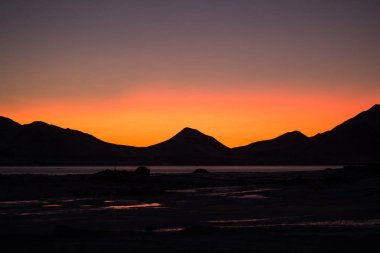 Dağ siluetlerinin üzerinde parlak renkli gün batımı 