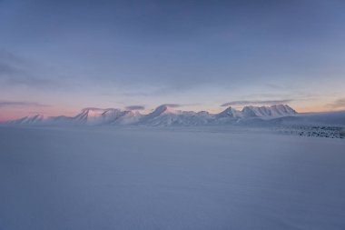 Pembe ve mavi tonlarda yumuşak karlı yüzey ve arka planda dağlar.