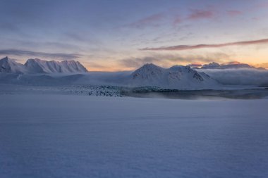 Pembe ve mavi tonlarda yumuşak karlı yüzey ve arka planda dağlar.