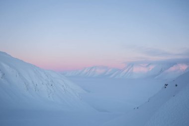 Karlı dağ zirveleri ve pastel tonlarda gün batımı.
