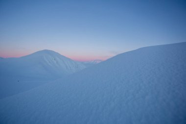 Karlı dağ zirveleri ve pastel tonlarda gün batımı.