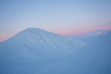 Karlı dağ zirveleri ve pastel tonlarda gün batımı.