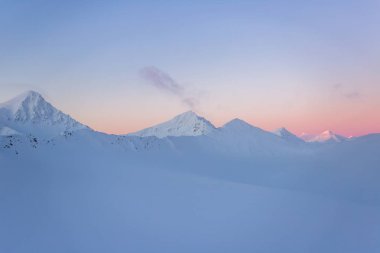 Karlı dağ zirveleri ve pastel tonlarda gün batımı.