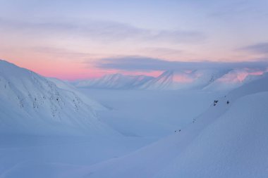 Karlı dağ zirveleri ve pastel tonlarda gün batımı.