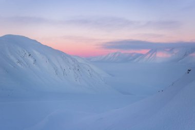 Karlı dağ zirveleri ve pastel tonlarda gün batımı.