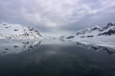 Sudaki yansımalarıyla karlı tepeler