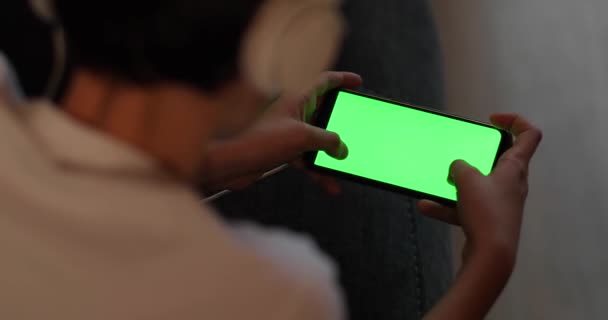 Back view close up of a teen hand using a smart phone with green screen on a couch at home. — Stock Video