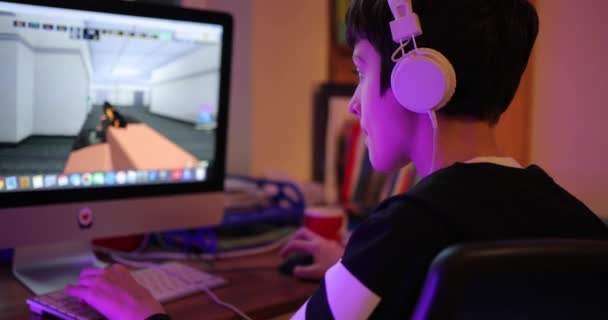 Професійний геймер, який грає в онлайн ігри турніри на ПК комп'ютері з навушниками. Хлопчик-підліток, який грає у відеоігри на комп'ютері в темній кімнаті, носить навушники та використовує клавіатуру. хлопчик — стокове відео