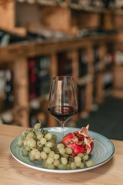 Glass of red wine in plate with green grapes and pomegranate