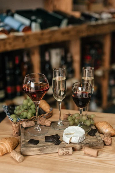 Glasses with red and white wine on wooden board with grapes, cheese and chocolate