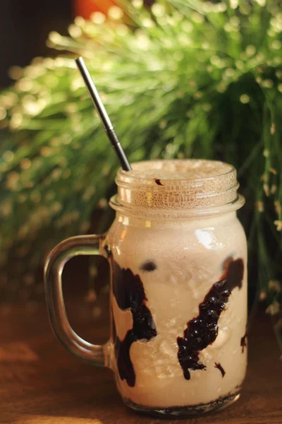 冷咖啡刨冰在玻璃罐子里用巧克力和泡沫在木桌与新鲜的草在背景上 — 图库照片