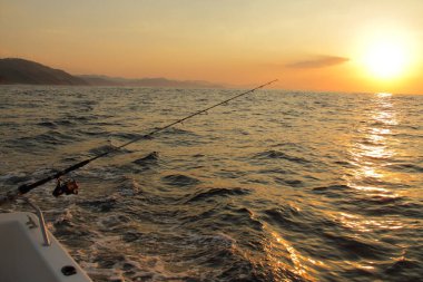 Balık oltası ve yem okyanusun üzerinde gün batımında, gün batımında teknede balık tutmak. 