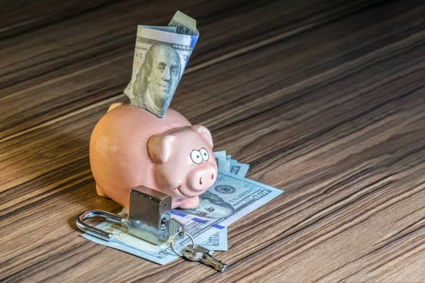 a piggy bank from which a hundred dollar bill looks out, and in front of it is an open door lock as a symbol of an open deposit