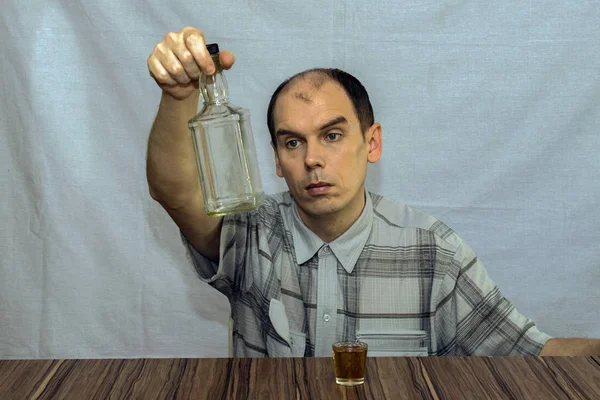 Man Sits Table Looks Empty Bottle Alcohol Front Him Glass — Stock Photo, Image