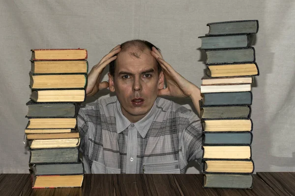 Ένας Άνδρας Κάθεται Μεταξύ Δύο Μεγάλες Στοίβες Βιβλία Κρατούσε Κεφάλι — Φωτογραφία Αρχείου