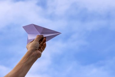 Bir elini gökyüzüne bir kağıt uçak arka planda tutuyor.