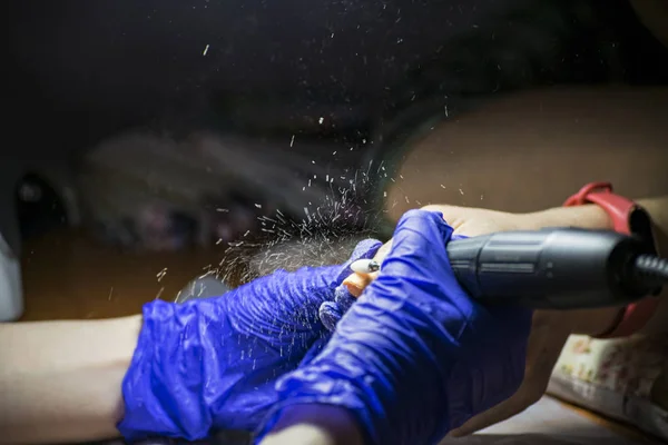 Manicurist removes old nail polish from nails with an electric machine.