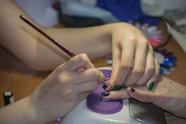 The manicurist applies the drawing with a brush on the nail.