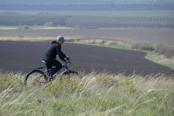 A woman on a bike rides over rough terrain.