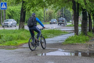 Ust-Kamenogorsk/Kazakistan - 05.21.2019: Yağmurdan sonra sokakta sırt çantası olan bisikletçi.