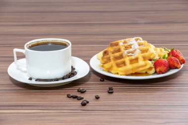 Viyana waffle pudra şekeri serpilir ve bal ve çilek ile sırılsıklam. Bir fincan kahvenin yanında.