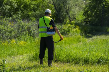 İşçi çimleri benzin budayıcı ile biçiyor..