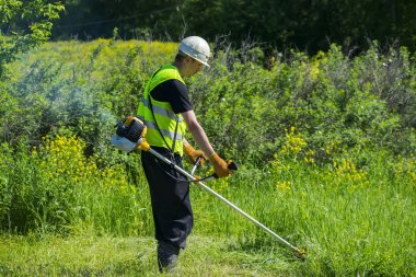 İşçi çimleri benzin budayıcı ile biçiyor..