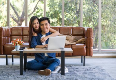Young lovers spend time together on holidays in the living room. Both are interested in studying online while the man typing keyboard of laptop computer.