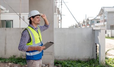 Güvenlik teçhizatında inşaat amiri gün ışığında bir şantiyede yeni evin gelişimini gözlemliyor. Güvenlik standardının sağlanması için tablet bilgisayardaki gelişmeleri kaydetti ve izledi..