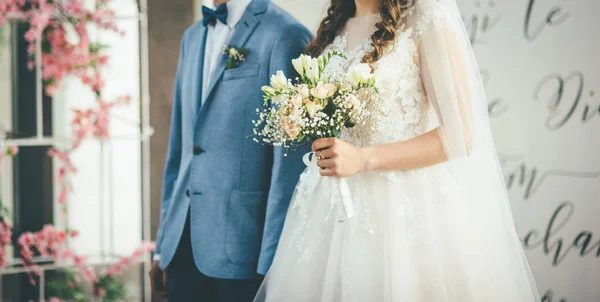 Braut und Bräutigam gehen zusammen mit Strauß in den Händen — Stockfoto