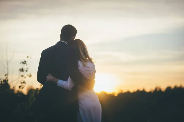 Milující svatební pár objímání při pohledu na západ slunce — Stock fotografie