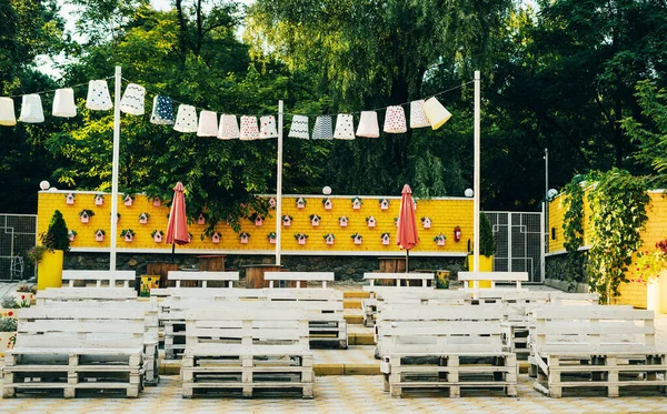 Outdoor venue. White benches on a background of a yellow wall with birdhouses and umbrellas.