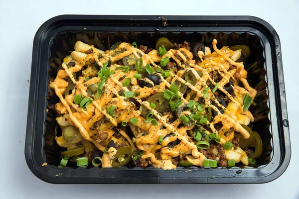 A high contrast Hero shot of a Take-Away Hot Loaded fries / chips with cheese, ground meat, olives, jalapeno, sauce & oregano, on a minimal white background with a 90 degree angle from zoomed vertical  perspective.