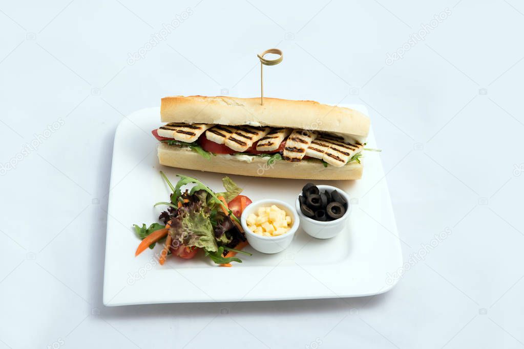 A high contrast Hero shot of a Grilled Halloumi cheese baguette with olives & salad on the side, on a minimal white background with a 60 degree angle from frontal zoomed perspective