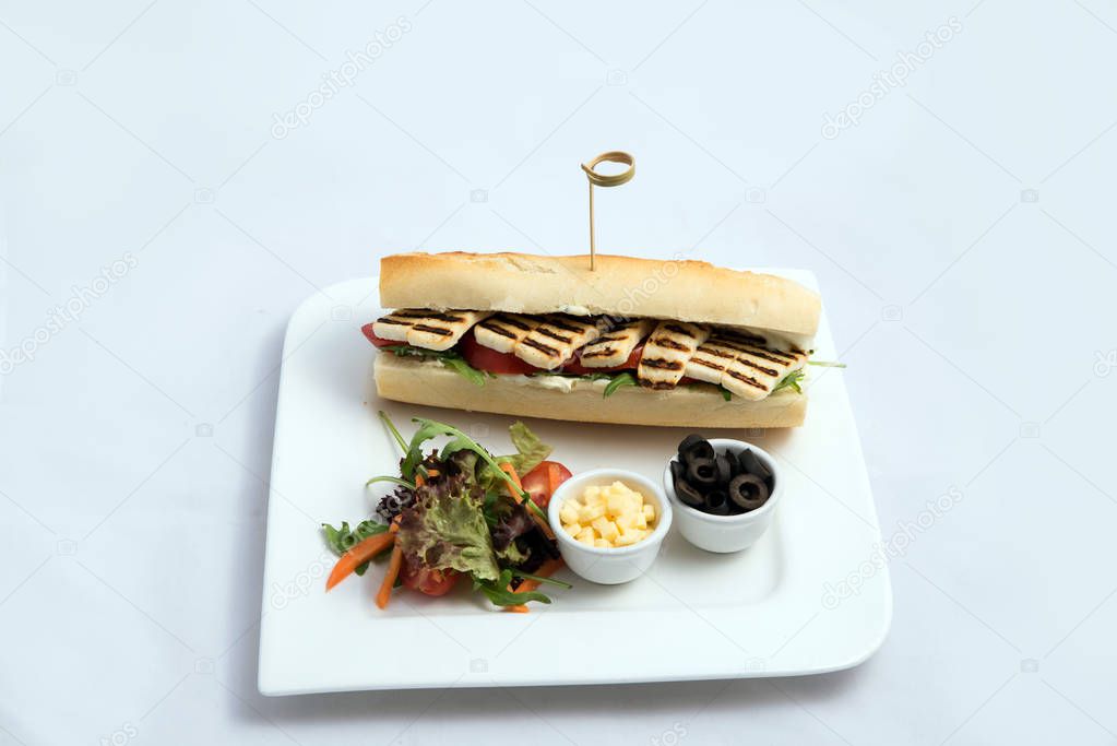 A high contrast Hero shot of a Grilled Halloumi cheese baguette with olives & salad on the side, on a minimal white background with a 60 degree angle from frontal zoomed perspective with space at the top for text inlay