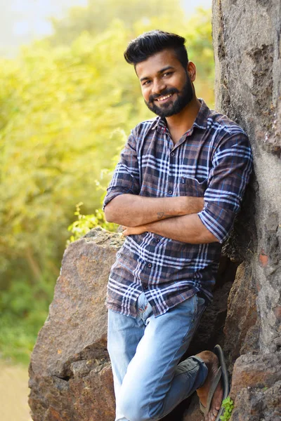 Modello maschile sorridente alla macchina fotografica poggiata sulla roccia. Mumbai — Foto Stock