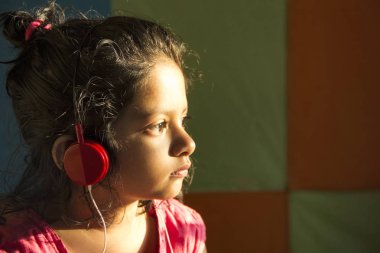 Yakın çekim küçük kız güneş ışığı, kırmızı renkli kulaklık Pune, Maharashtra, Hindistan ile müzik dinlemek