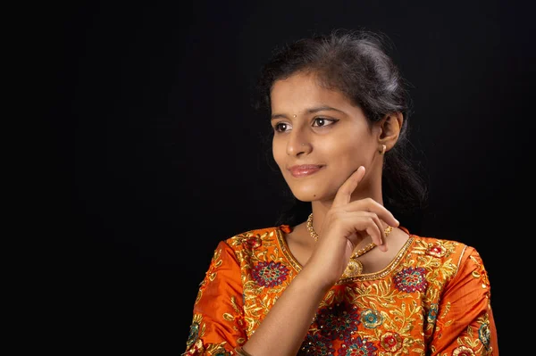 Portrait of a happy young Indian girl smiling on black background with hand on chin
