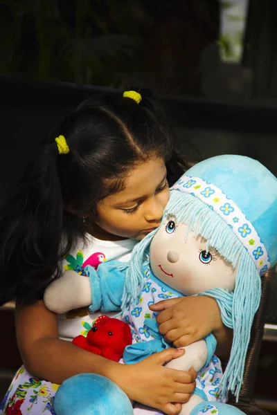 Pequeña niña india sentada y besando su muñeca dentro del jardín, Pune . — Foto de Stock