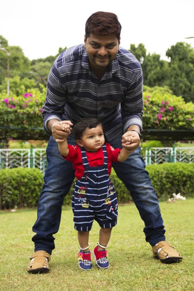 Vader helpt zijn peuter zoon te lopen in een tuin, Pune, Maharashtra. — Stockfoto