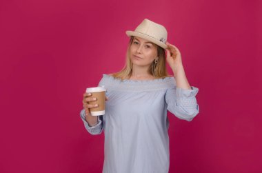 Mavi elbiseli onun elinde kahve ile hasır şapkalı kadın. Pembe studio arka plan üzerinde izole. Genç hippi kız. Yaz tatili, eğlence ve tatil kavramı. 