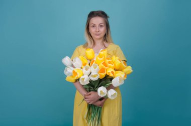 Sarı elbiseli kadın çiçek elleri üzerinde mavi arka plan izole içinde Grup ile. Renk kavramı. Yaz dönemi, bahar çiçek açan kavramı. Beyaz ve sarı laleler buket. Kopya alanı.