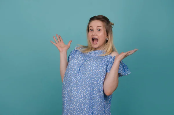 Surprised and excited women spreads out her hands. Shocked and scared pretty girl isolated on blue background. Expressive facial expression. She is amazed and raise her arms