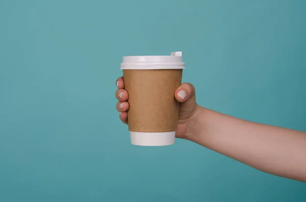 Coffee cup in woman hand isolated on blue background. Female hand with paper cup. Mockup of female hand holding a coffee paper cup. Copy spac